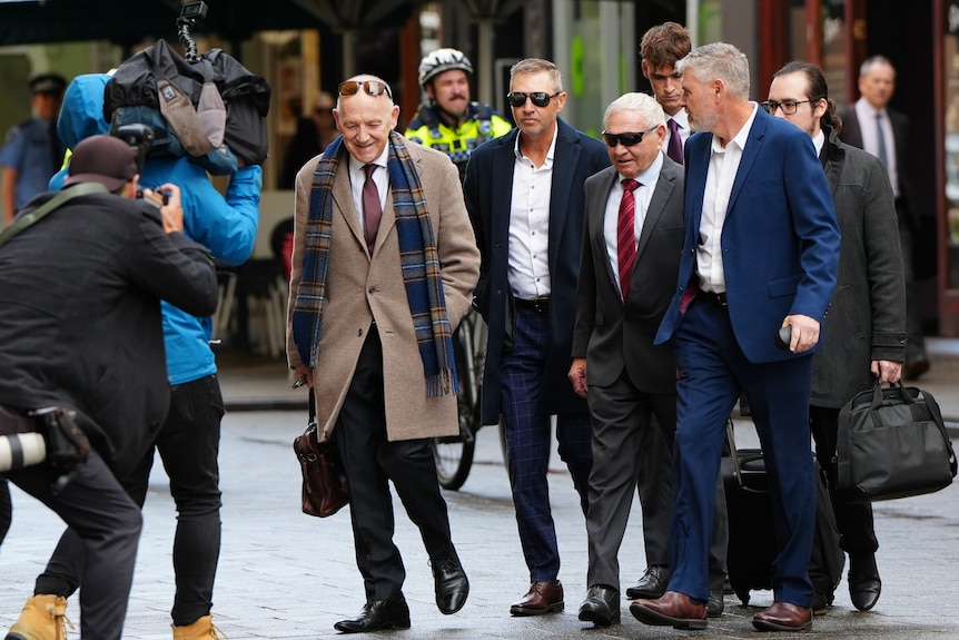 A group of people in suits walk across a busy city street