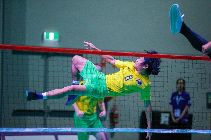 Australian sepak takraw player spiking ball over net in mid-air.