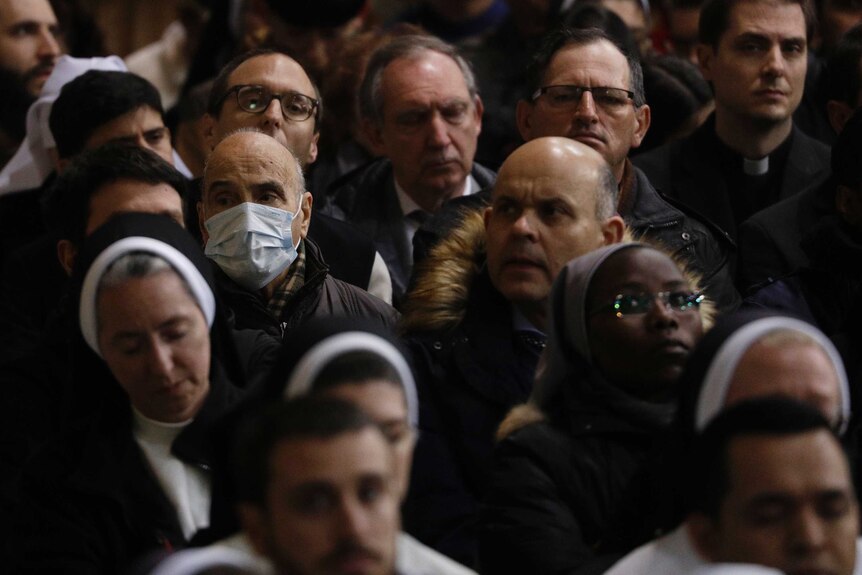 A man in a crowd wearing a surgical mask