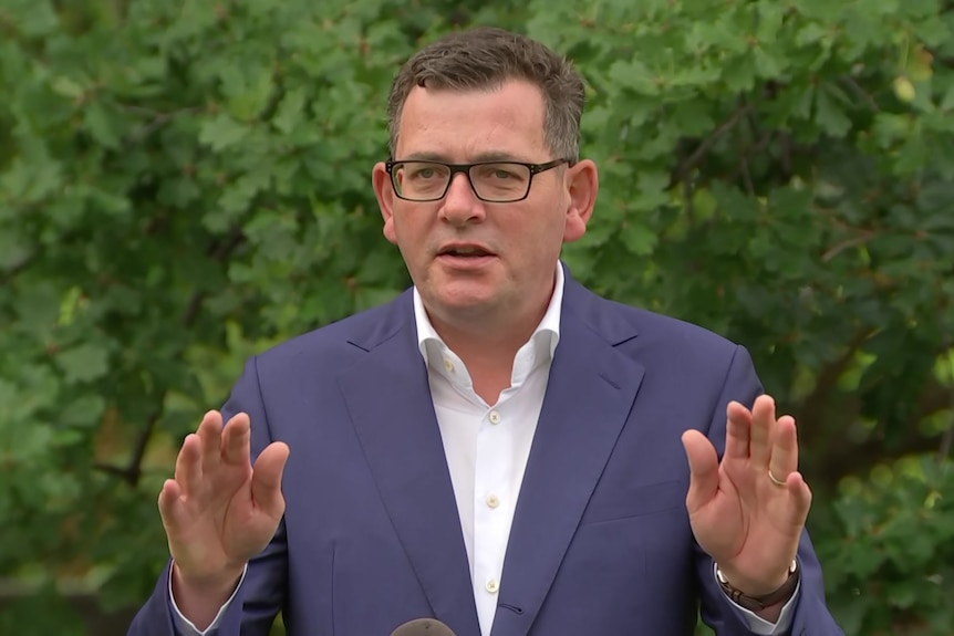 A man in glasses and a blue suit in front of trees