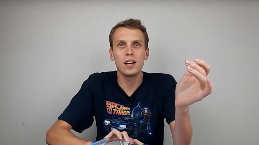 A man sits at a desk with a robot in his hand as he talks.