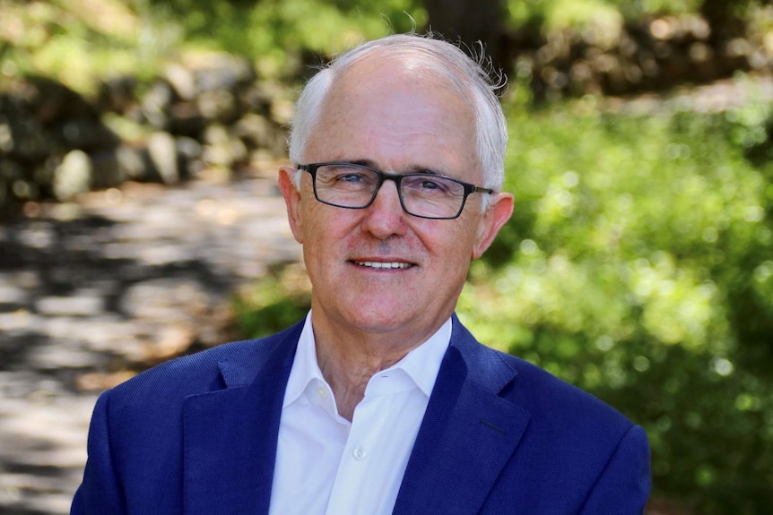 A man with white hair and glasses smiles