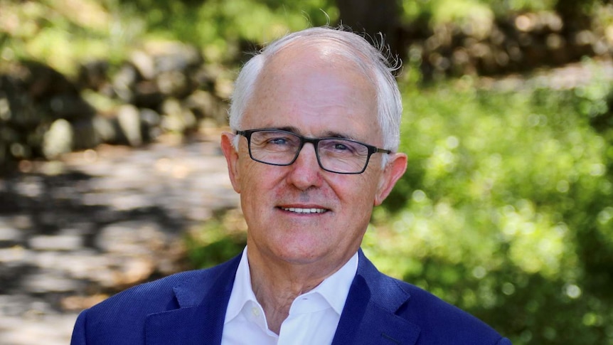 A man with white hair and glasses smiles