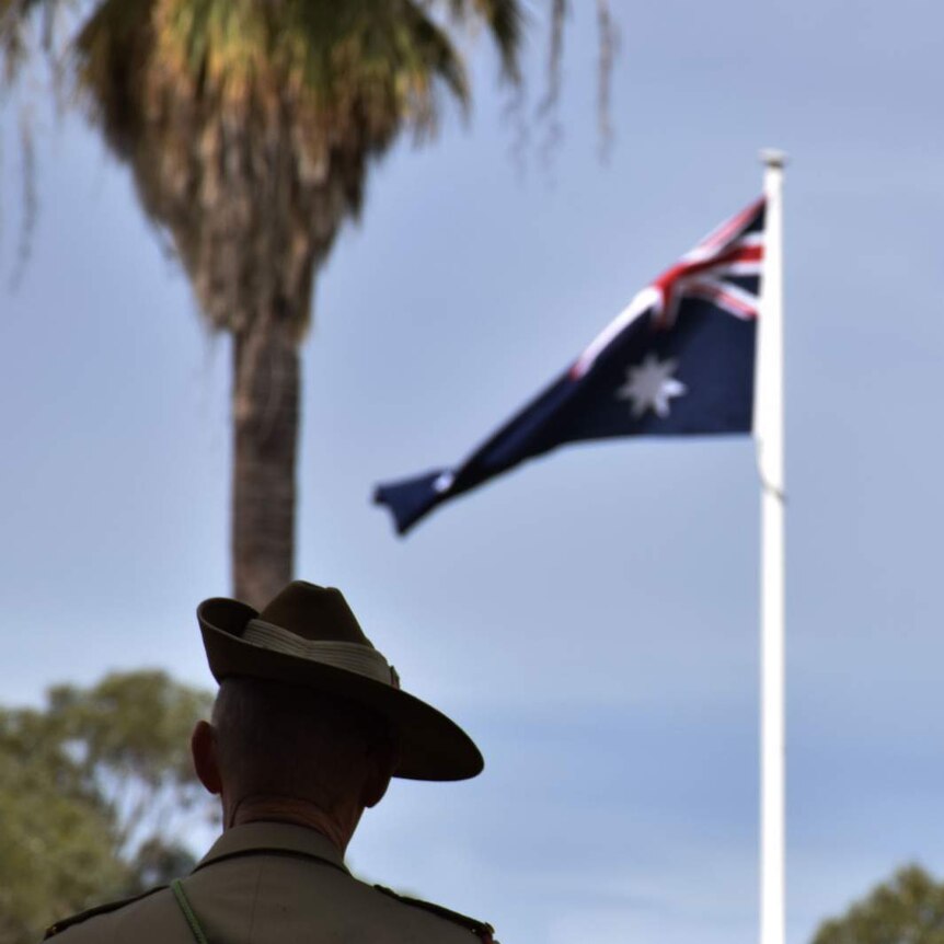 A soldier is pictured from behind, with an Australian flag in the distance, which flies next to a palm tree in Perth, Australia.