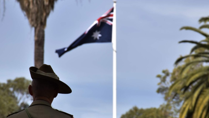A soldier is pictured from behind, with an Australian flag in the distance, which flies next to a palm tree in Perth, Australia.