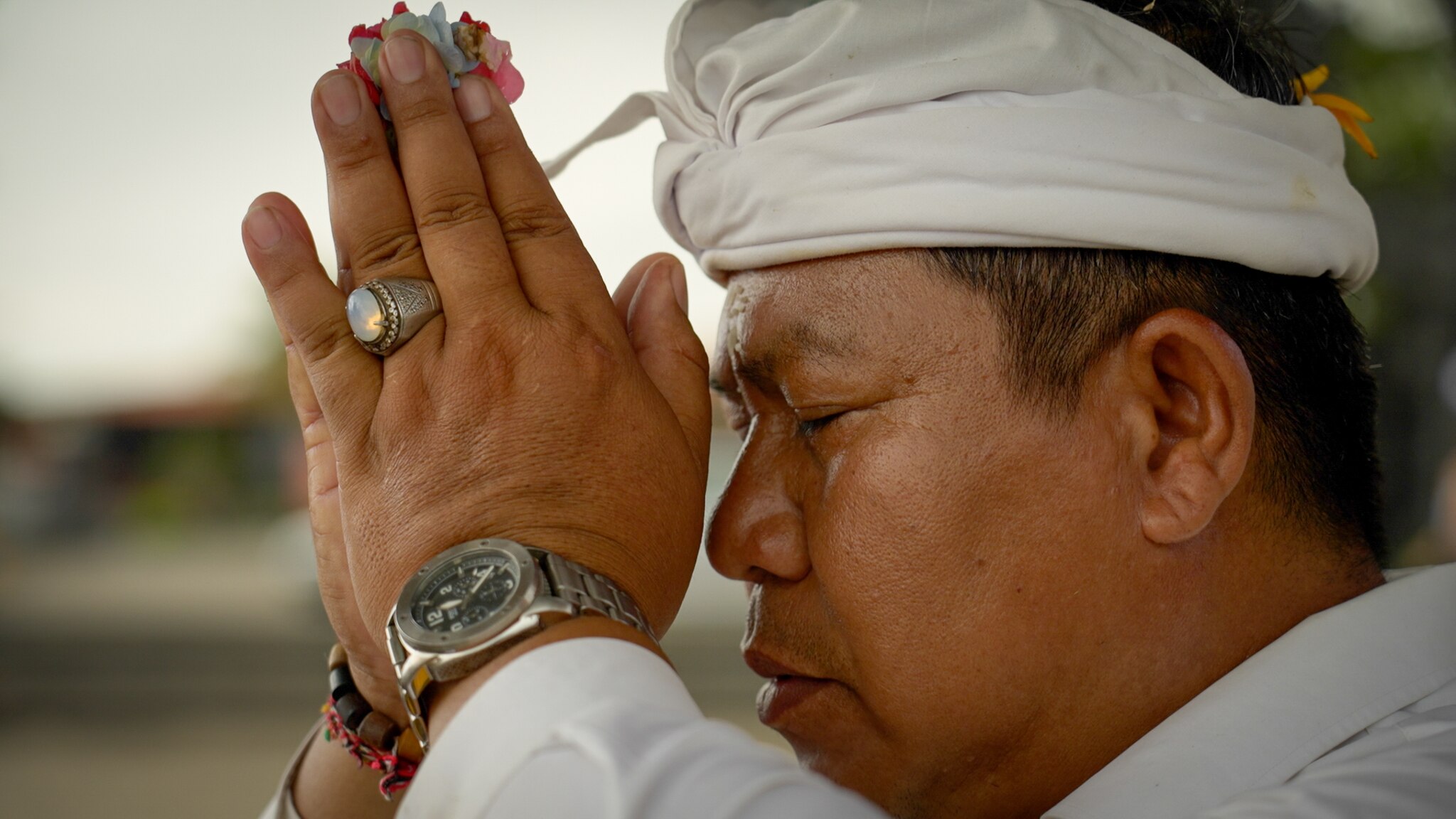 An Indonesian man holds a flower between his hands, which rest against his face in prayer