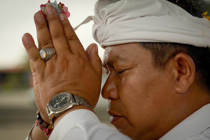 An Indonesian man holds a flower between his hands, which rest against his face in prayer