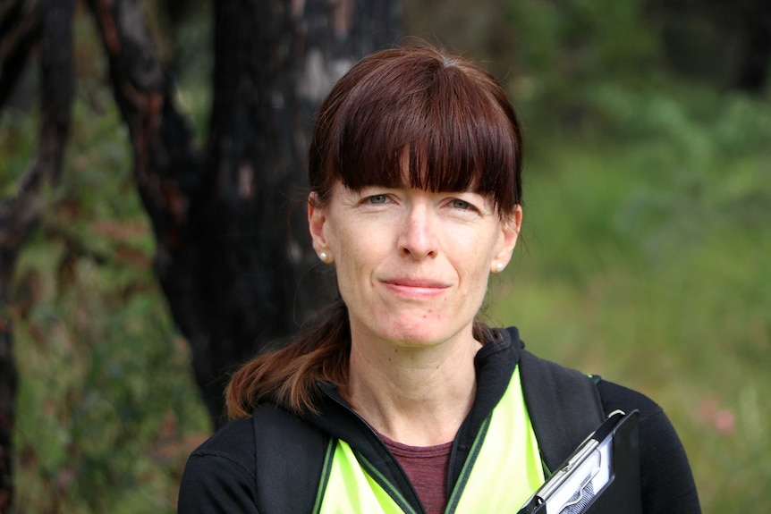 Murdoch University biologist Dr Rachel Standish looks at the camera, wearing hi-vis and holding a clipboard.