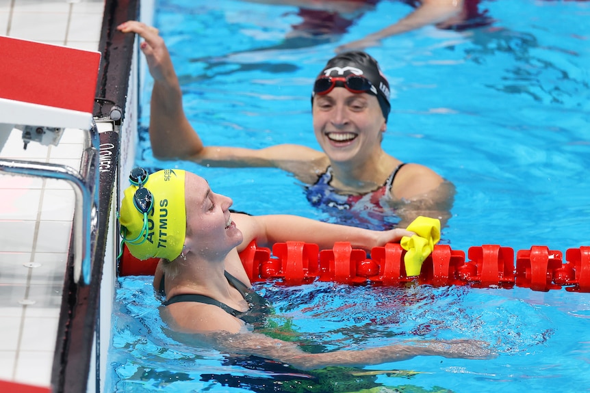 A woman wearing a yellow swimming cap next to another woman in a black swimming cap in a pool