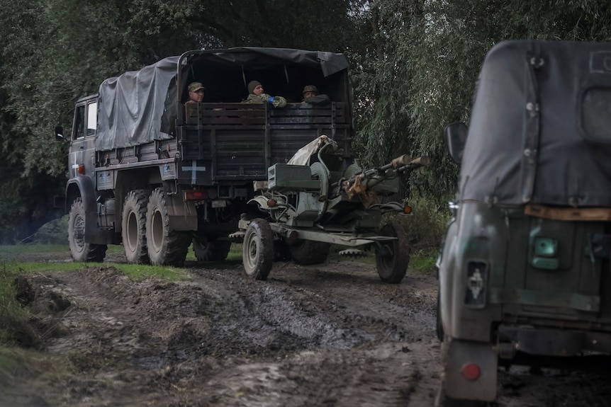Rear view of Ukrainian servicemen riding on the back of military vehicles, towing weapons through mud.