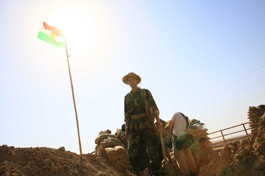A Kurdish fighter walks along the frontline with the Islamic State in Kirkuk as a Kurdish flag flies in the background