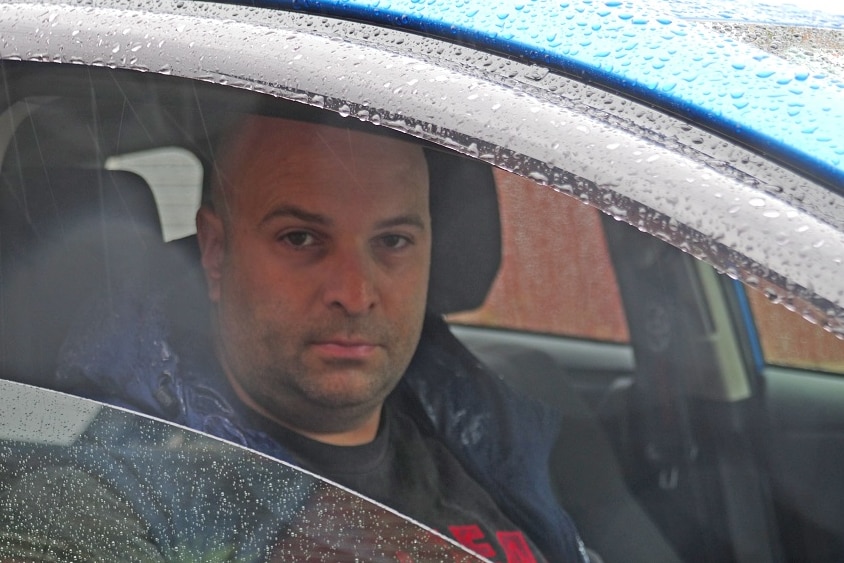 Maurice Cali looks out from the driver's window of his blue car.