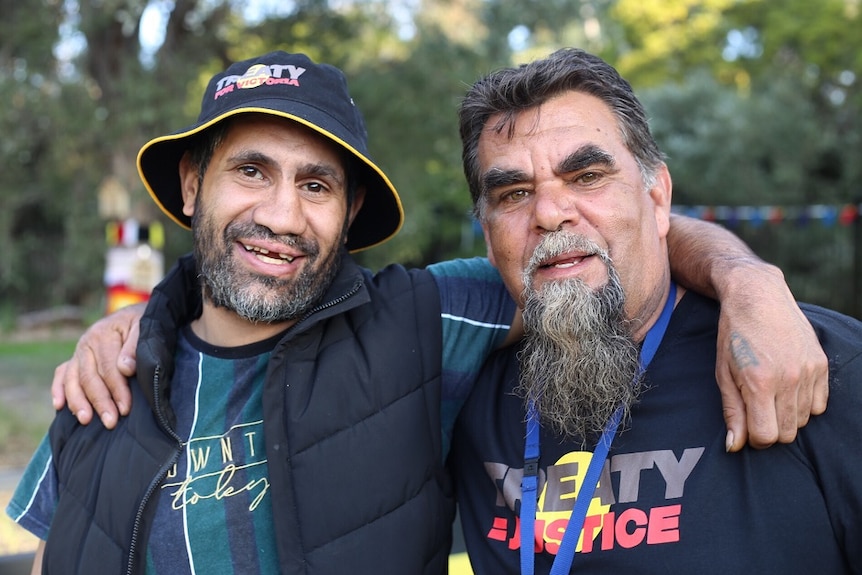 Reg Edwards and Shane Clarke smile as the stand with arms around each other's shoulders in a park.