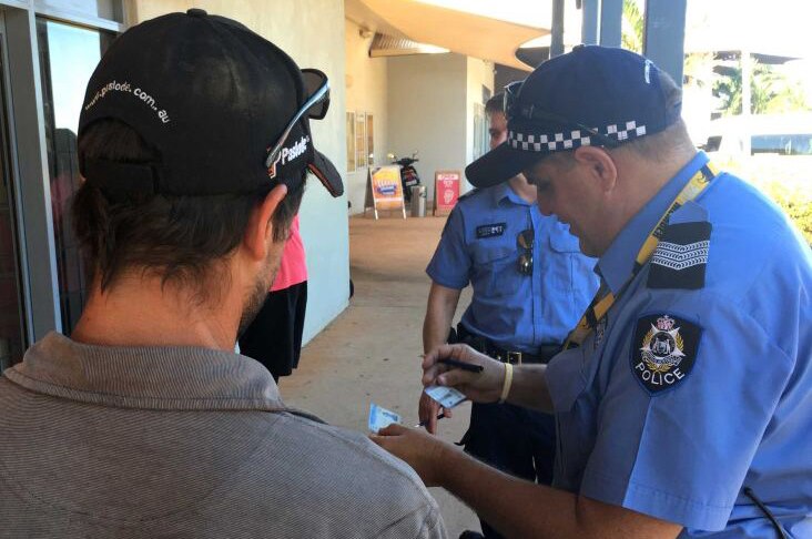 A man with his back turned has his ID checked by two police officers on the street.