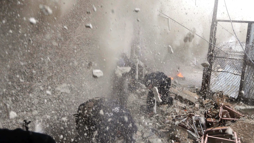 Free Syrian Army fighters run for cover as a tank shell explodes on a wall next to them.