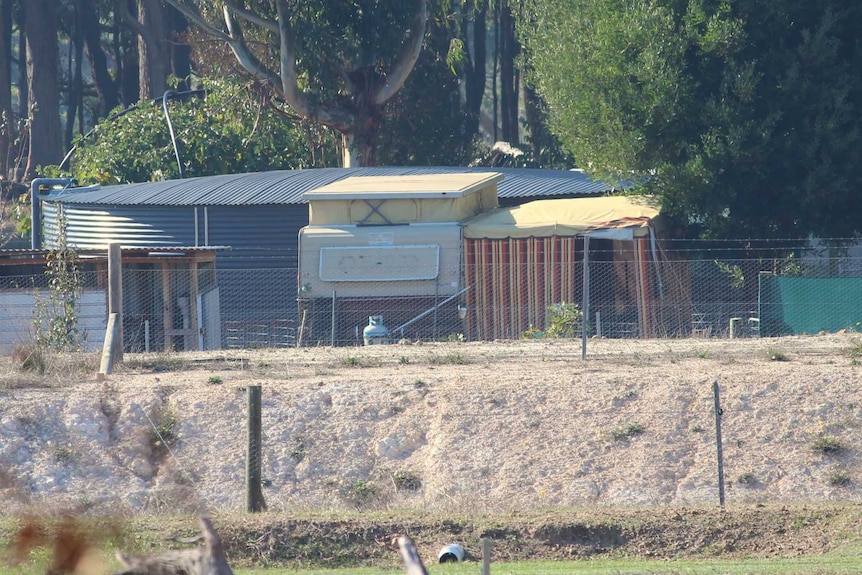 A rural property with a water tank and caravan visible among trees.