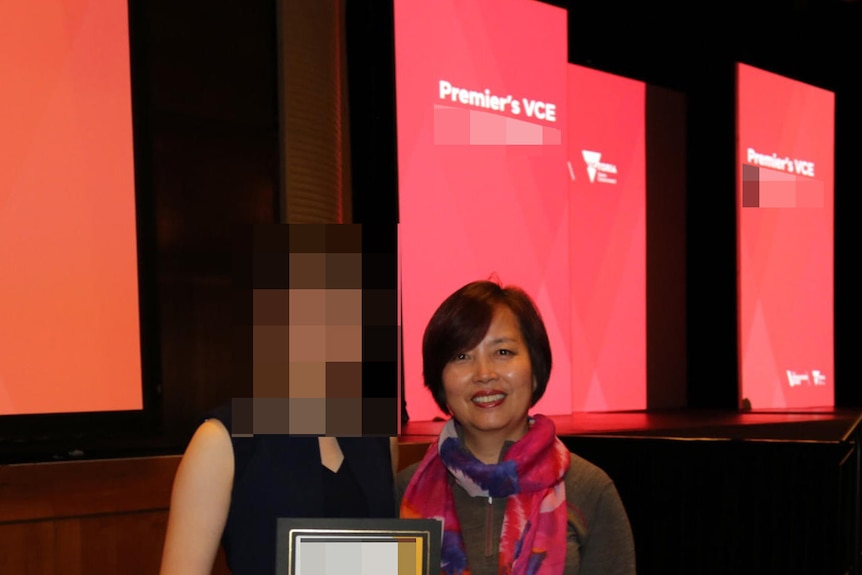 A woman smiles at the camera next to a student holding her award.