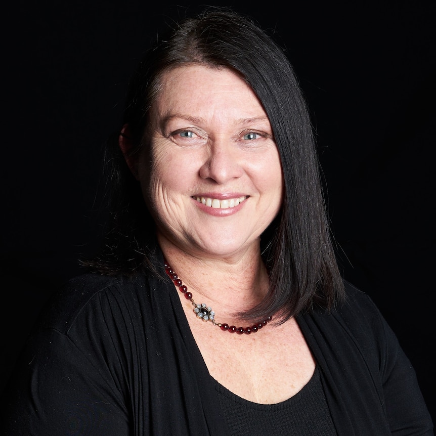 A head shot of Monica Penders smiling with a black background