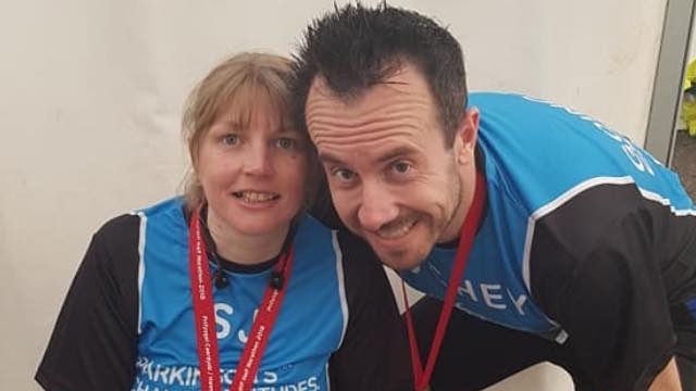 A woman and a man wearing blue singlets, smiling at the camera.