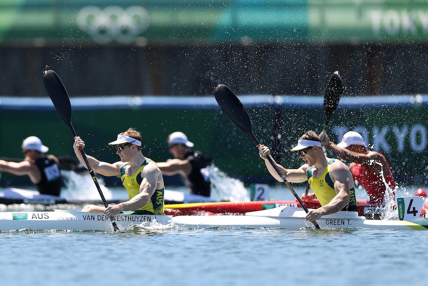 Two men in green and gold in a double kayak racing.