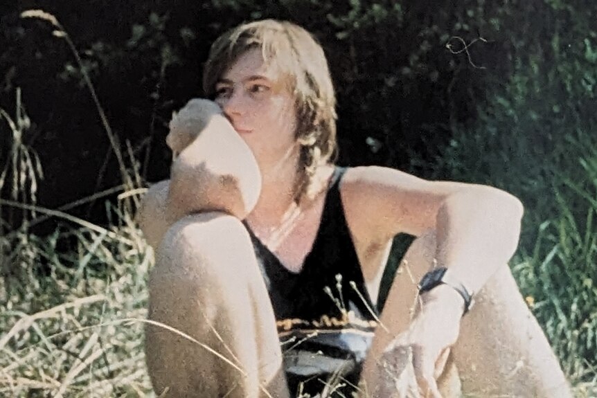 Teenage male sitting in grass, looking away from camera, 1989.