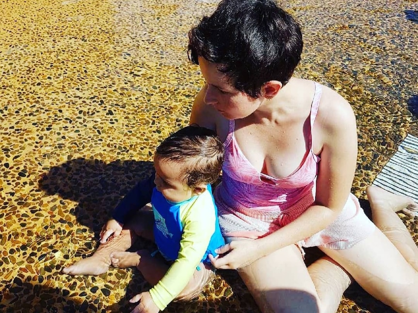 Emma in a pool, holding a baby.