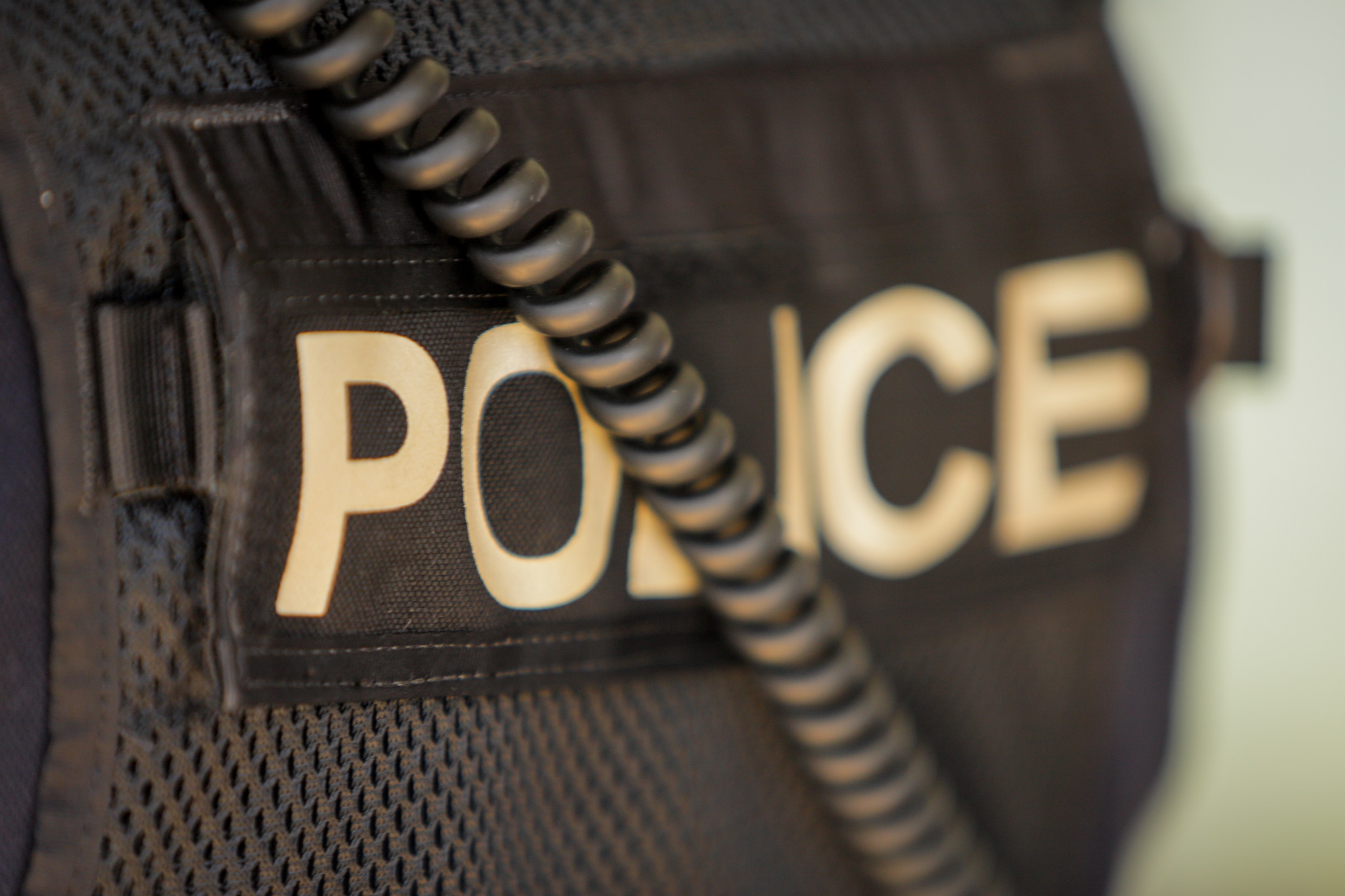 A close up of the back of a police officer. The black vest reads: POLICE.