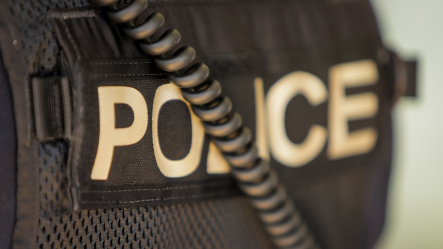 A close up of the back of a police officer. The black vest reads: POLICE.