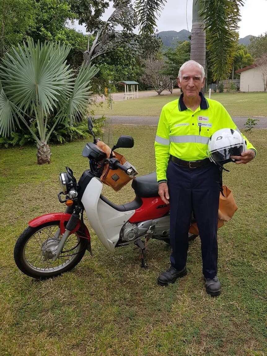 man in high viz stands holding helmet in front of motorbike