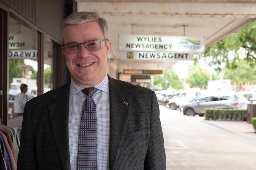 A man in a grey suit wearing glasses looks at the camera with the main street of Temora in the background.