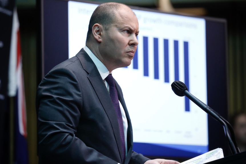 Treasurer Josh Frydenberg in a suit in front of a TV screen