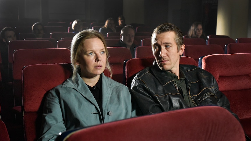 A film still of Alma Pöysti and Jussi Vatanen, sitting in a cinema. Vatanen is looking at Pöysti who is looking at the screen.