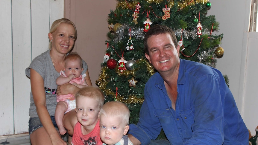 Sarah and Brook McGlinchey sitting on their living room floor in front of a decorated Christmas tree with their three children.