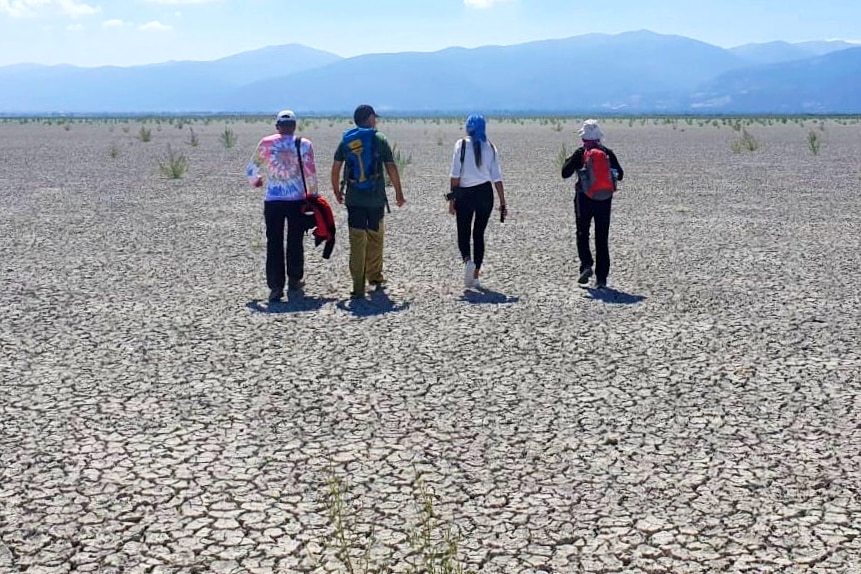 Four people walk across a field of dry cracked earth.