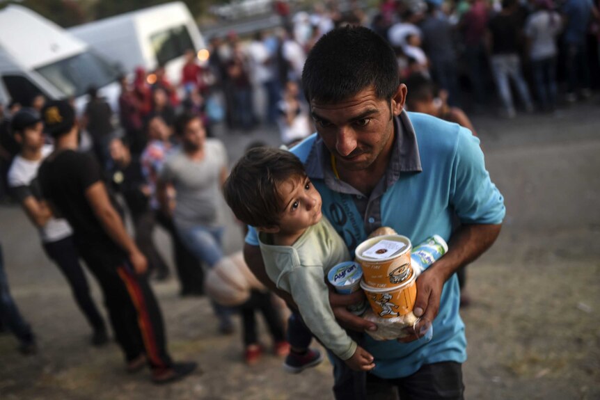 A Syrian man carries packaged food as he cradles his child in his arms