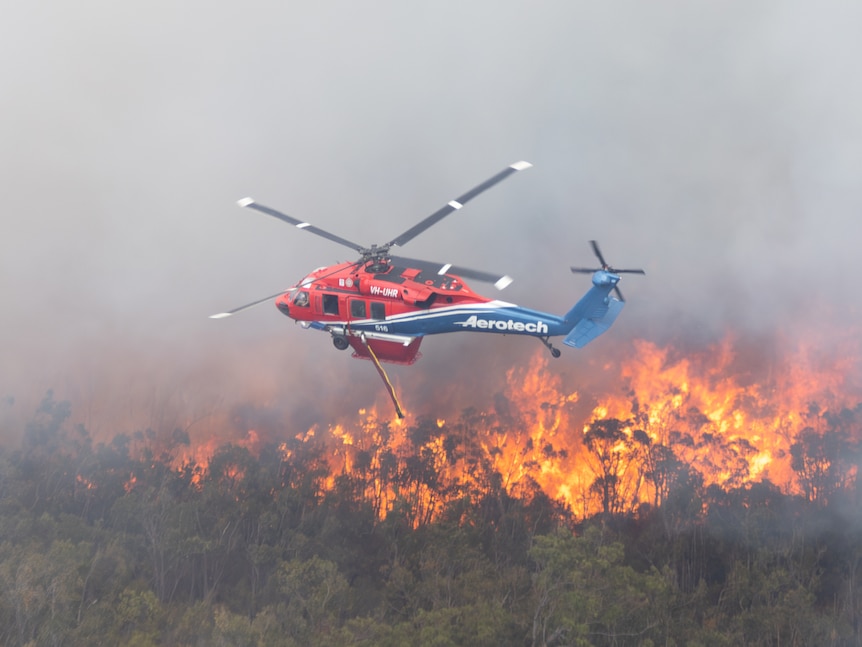 A helicopter dropping water onto a bushfire.