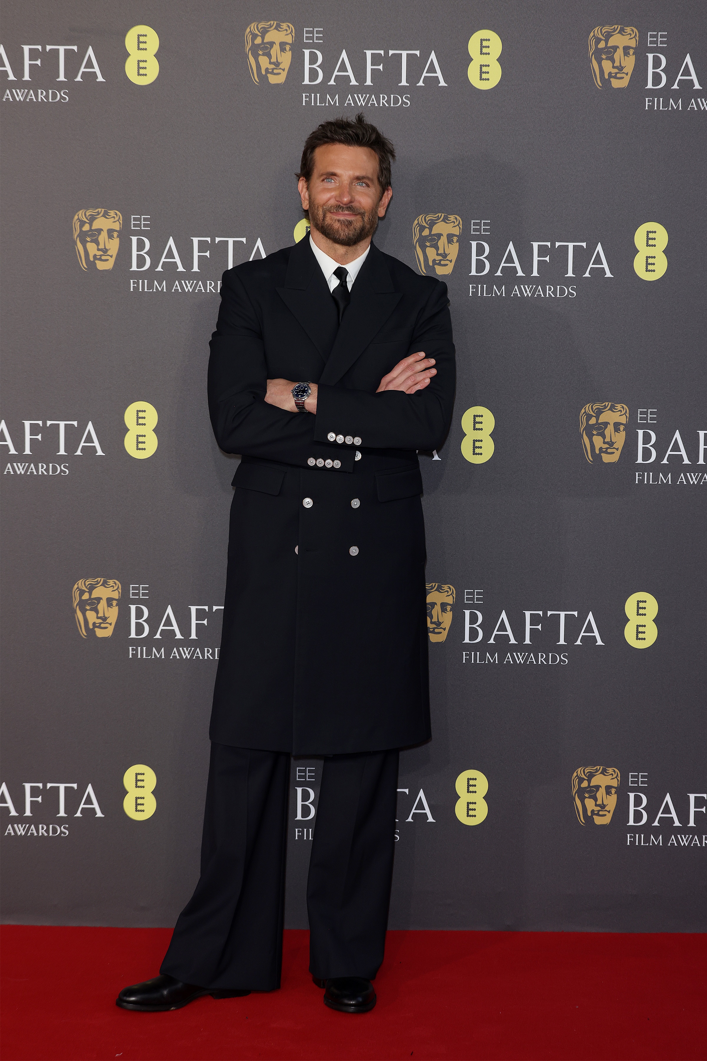 Bradley Cooper in a black suit with a long coat on the red carpet