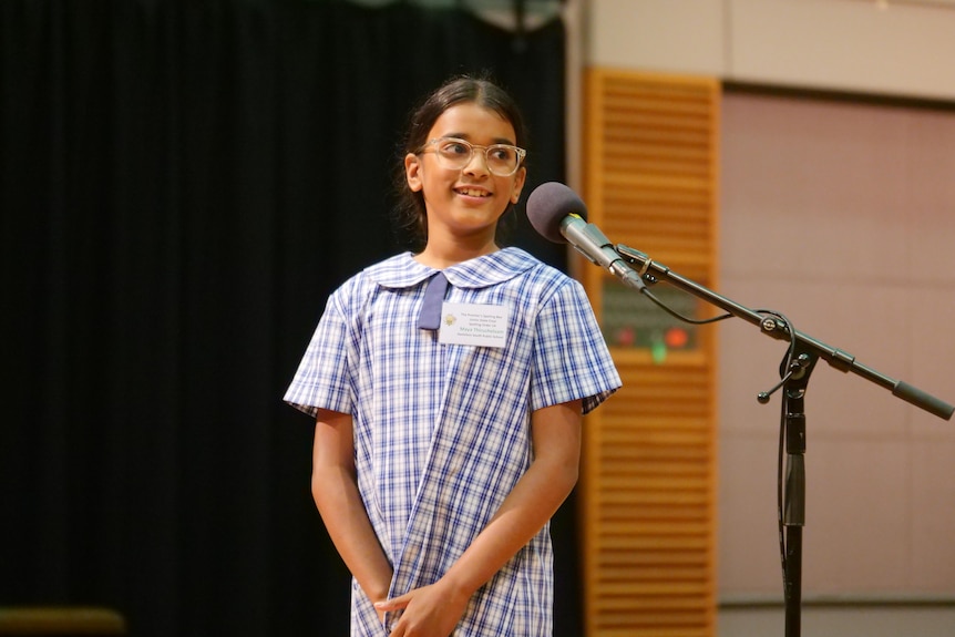 A young girl smiles standing at a microphone