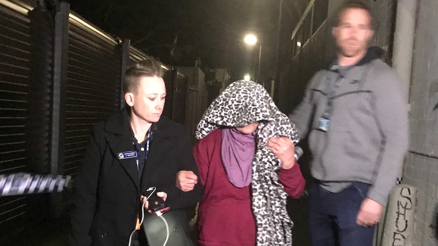 A woman with head covered in leopard-print fabric led to a car by police in Sydney's Surry Hills at night