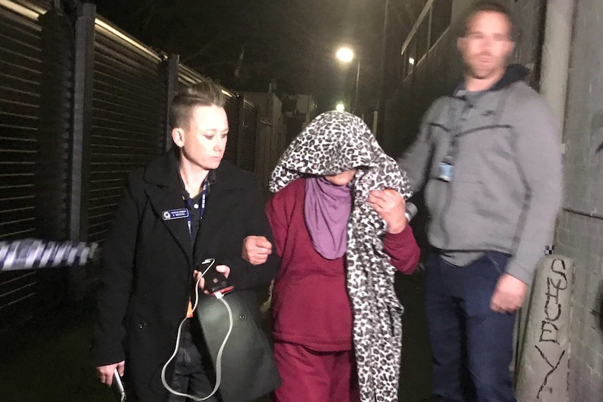 A woman with head covered in leopard-print fabric led to a car by police in Sydney's Surry Hills at night