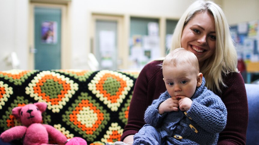 Jasmine Smith with her son Lawson sitting on her lap wearing the hand knitted blue cardigan she made for him