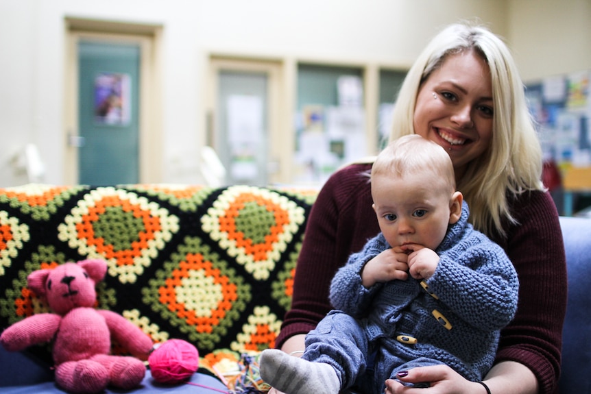 Jasmine Smith with her son Lawson sitting on her lap wearing the hand knitted blue cardigan she made for him