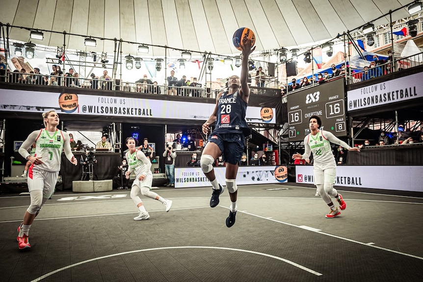 A shot from a low angle shows Migna Toure come in for a lay-up with the court and stands in the background.