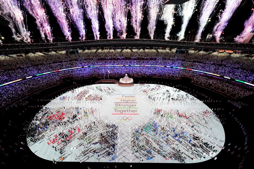 Fireworks explode of the Olympic stadium full of athletes.