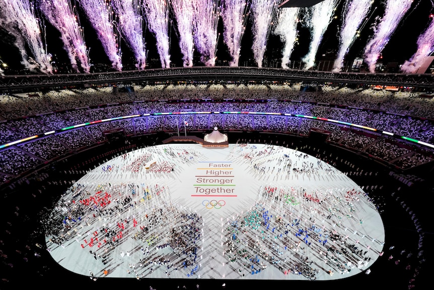 Fireworks explode of the Olympic stadium full of athletes.