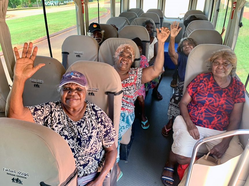 Six people sit on a bus, waving and smiling