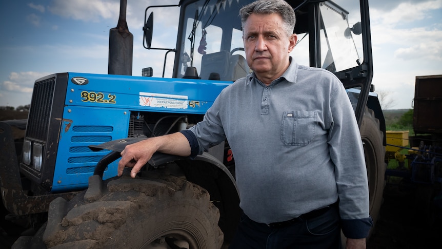 A man with grey hair and wearing a grey shirt stands next to a tractor.