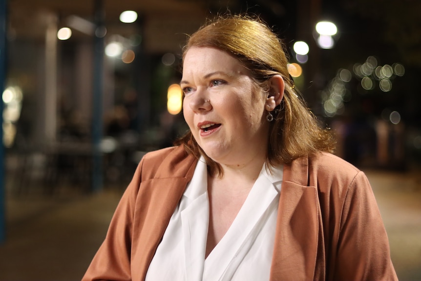 A woman with ginger hair, formally dressed, sitting down as if in an interview.