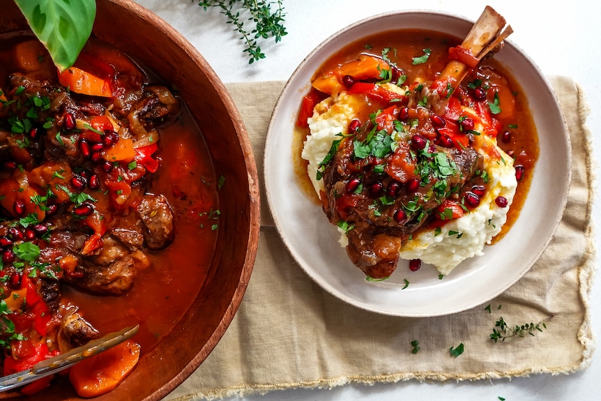 Slow-cooked lamb shanks with pomegranate sauce in a pot, and also in a bowl served atop a heaping of mashed potato.