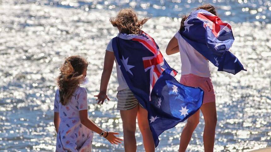 three children draped in Australian flags stand near the water
